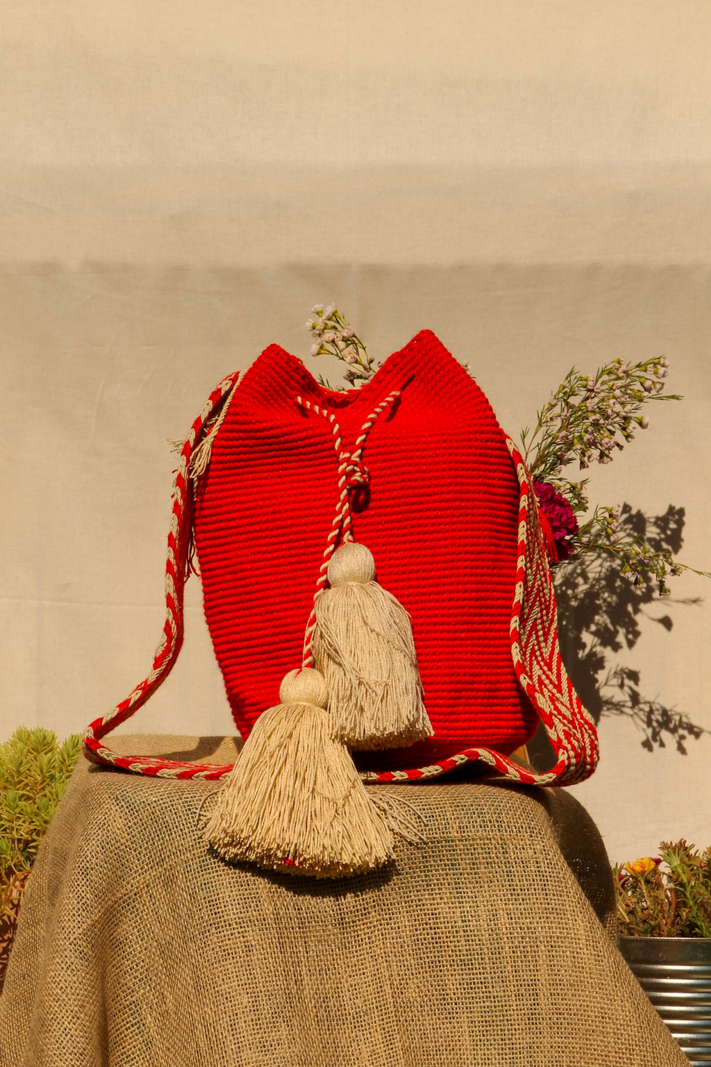 Red handwoven wayuu bag with tassels on a textured surface with a blurred natural background
