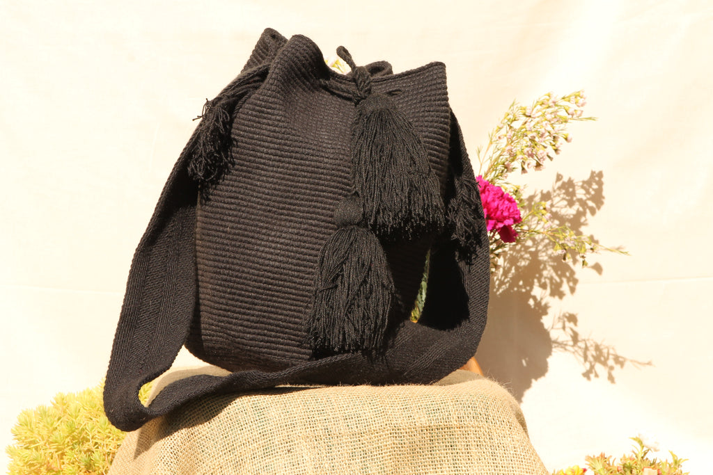 Black handwoven wayuu bag with tassels on a stone surface with a natural background