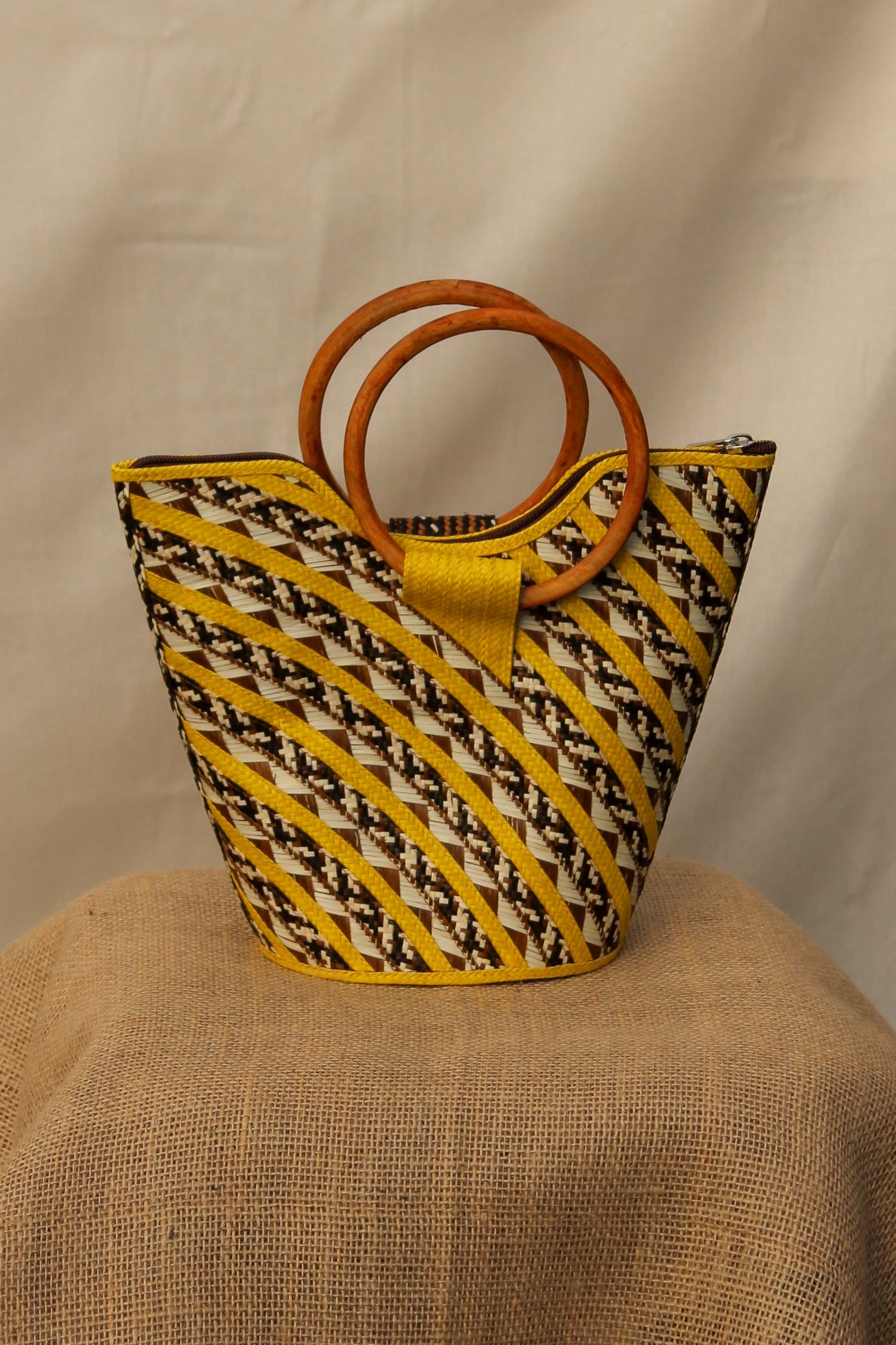 Yellow woven handbag with wooden handles on a beige fabric background